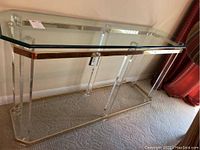 Front view of the glass console table showing glass top and acrylic legs with metal trim on edges.