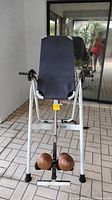 Full view of the inversion table from the front showing the padded backrest, white frame, and ankle locks with weights.