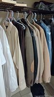 Side view of men's dress shirts and jackets hanging on a rack, showing variety of colors and fabrics.