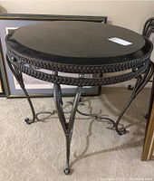 Full view of the round table showing the black granite top and metal decorative base on carpet.