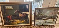 Photo showing both framed paintings side by side near a window with stained glass, the left painting depicts a boy, dog, and horse, the right painting depicts a snow-covered cabin landscape.
