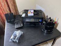 Full lot overview on black desk showing Brother printer, keyboard, speakers, desk organizer with pens, and power cord.