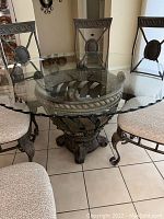 Close-up of the ornate composite metal base of the table and glass top with chairs arranged around it.
