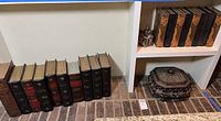 Photo showing 11 antique style decorative books placed on and in white shelving with two decorative ornate storage boxes.