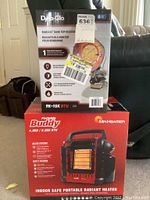 Photo of the boxed Dyna-Glo Radiant Tank Top Heater and Mr. Heater Portable Buddy heater stacked and displayed in a room.