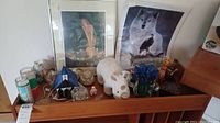 Wide view showing multiple items on wooden dresser including cat figures, stained glass lamp, candles, art prints, and bird figurines.