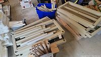 Overview of disassembled beige shelving components including vented shelves, cylindrical rods, and frame parts.