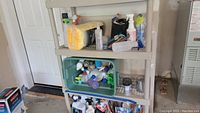Photo showing plastic shelving filled with cleaning products including bottles, microfiber cloths in packaging, sprayers and a bucket with cleaning tools.