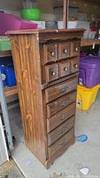 Full side view of the tall wooden dresser showing its seven drawers and dark brown finish with visible wear and dirt.