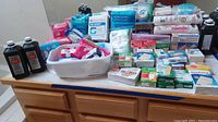 Full view of the lot arranged on a bathroom counter and dresser showing multiple medical supplies, including hydrogen peroxide, maxi pads, bandages, gauze, cotton balls, and kleenex packs.