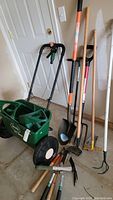 Full view of Scott's AccuGreen 3000 spreader, shovel, rakes, and some hand tools against wall and door.