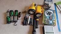 Multiple flashlights of various types including large yellow, green and black LED, and smaller silver and black flashlights along with disk light packaging and Philips motion light case on beige carpet.