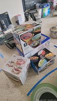 Photo showing boxed Mikasa Marrakesh bowl set with 6 bowls and lids, stacked with other boxed kitchen items.