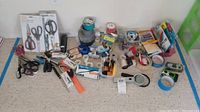 Wide view of assorted office supplies on carpet including scissors, tape rolls, pens, stapler, disposable cameras, clips and packing supplies