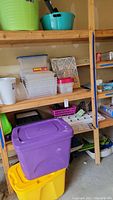 Plastic storage containers and collapsible totes on wooden shelves, including purple and yellow totes.