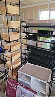 Photo showing the eight-tiered black metal basket storage rack with wicker baskets and two black metal rolling carts, one still in box.
