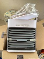 Arctic Air Ultra evaporative air cooler showing front grill and open box packaging around it.