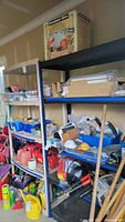 Black and blue metal shelving unit with four solid shelves loaded with various items including cardboard boxes, plastic containers, and tools.