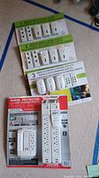 Overview of three wireless remote control outlet sets in white and one package of CyberPower surge protector three pack with USB ports, all new in box.
