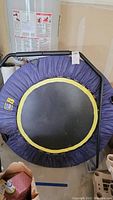 Top-down view of the mini trampoline showing purple fabric cover, yellow trim, and black jumping mat with visible dirt and smudges.
