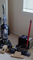 Full view of Dirt Devil upright vacuum cleaner with clear purple dustbin and Dyson vacuum parts and box on the floor.