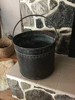 Side view of large antique arts and crafts pot with iron handle, showing patina and studded border details.