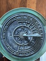 Top-down photo of brass sundial showing Roman numerals, compass rose, and gnomon shadow indicator.