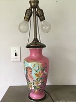 Full view of the porcelain lamp showing the pink and blue hand painted body with brass top and dual bulb sockets.