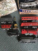 Top-down photo showing multiple red Lionel train cars, black freight cars, a red locomotive, and part of the cardboard tunnel and box with track sections.