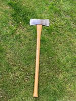 Full length of the axe laid on grass showing the wooden handle and double axe head.
