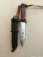 Full view of knife out of sheath showing polished blade, brown handle, and sheath with leather strap.