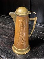 Front side view of copper and brass stein pitcher showing embossed geometric pattern and domed brass lid with spout.