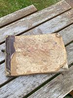 Front cover of map book showing worn cardboard cover with faux leather reinforcements and cord binding.