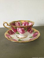 Side view of Royal Albert tea cup with pink rose floral pattern and gold rim and handle, displayed on matching saucer