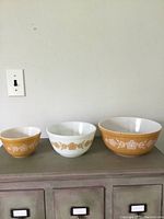 Set of three Pyrex mixing bowls displayed side by side showing graduated sizes and yellow and white floral patterns.
