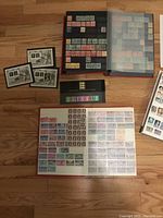 Stamp albums and loose pages with hundreds of stamps from multiple countries including Canada, USA, and Britain laid on a floor.