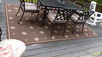 Large brown outdoor area rug with beige patterns under patio table and chairs on deck