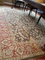 Photo showing coffee-colored area rug with paprika red border and floral vine pattern under dining table legs.