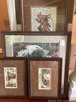 All four framed prints stacked against wall showing top horse print, middle eagle scene, and two small camouflage prints at base
