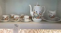 Full tea set displayed on a shelf showing cups, saucers, tea pot, creamer, sugar bowl, luncheon plates, and serving platter with Aynsley Cottage Garden pattern.