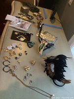 Overview of items on table: multiple jewelry pieces including earrings, rings, pins, feather hair combs and face masks displayed on a white surface.