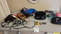 Overview of display on gray table showing sunglasses, cases, belts, necklaces, cufflinks, scarves, and other accessories.