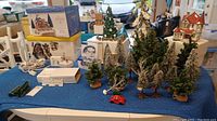 Overview of all items on blue cloth, showing the trees, miniature buildings, figurines, mailbox, fire hydrant, fencing, and original boxes.