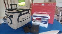 Overall lot: sewing machine on blue pad, red Husqvarna Viking Embroidery box, beige/black carry bag, foot pedal and media drive
