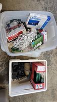 Top view of bin containing multiple boxes of Christmas lights, loose white lights, green extension cords, and an outdoor spotlight.