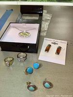Photo of assorted jewelry including two large rings, turquoise earrings, amber earrings in a card, and a Seahawks pendant necklace in a box