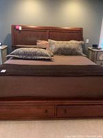Assembled king bed frame with headboard, footboard with drawers, side rails and bedding in room