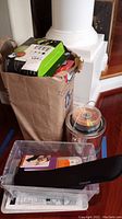 Paper bag filled with various printer ink cartridges and a plastic bin with office supplies and CD spindles visible behind.