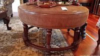 Overall front view of round ottoman showing leather seat and carved wood base