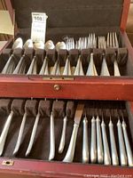 Overall view of the pewter flatware set inside a brown felt-lined wooden box organized in compartments.